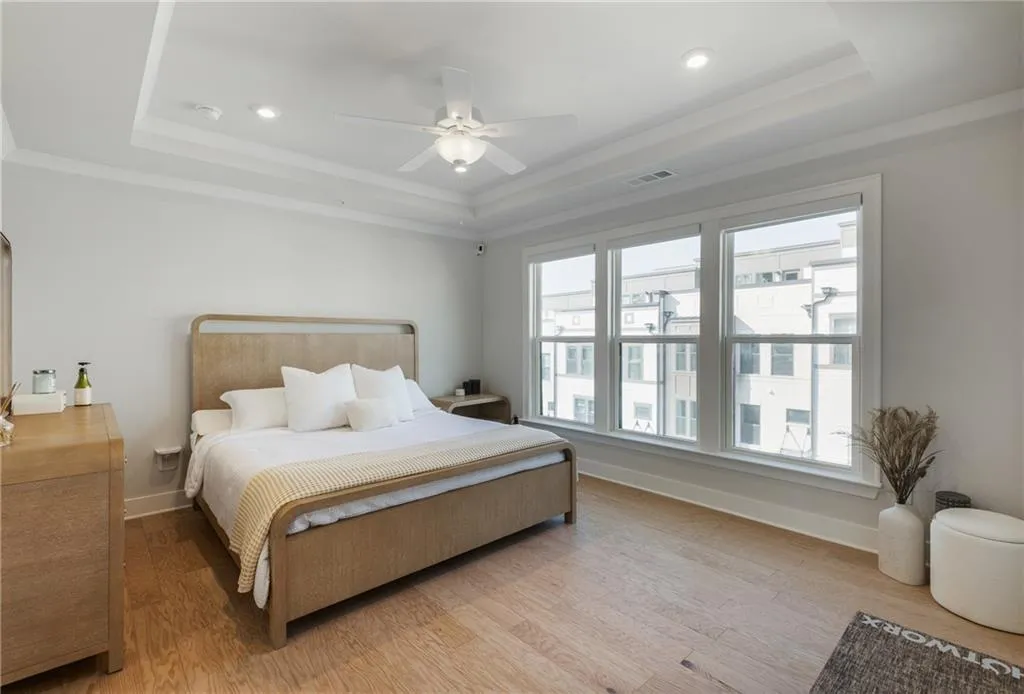 Bedroom featuring a raised ceiling, light wood-type flooring, a ceiling fan, ornamental molding, and recessed lighting