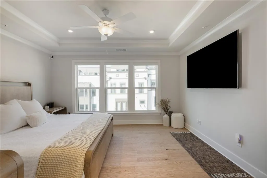 Bedroom with light wood finished floors, a raised ceiling, ceiling fan, recessed lighting, and ornamental molding