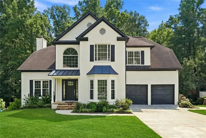 Two-story residence featuring a white brick exterior, black trim accents, a two-car garage, a covered entry with stone steps, and a bay window
