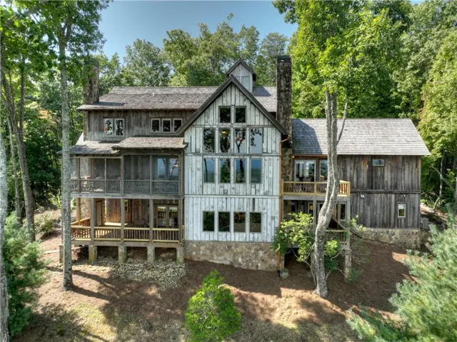 Multi-level residence featuring extensive wood siding, multiple decks, a stone foundation, and a prominent stone chimney