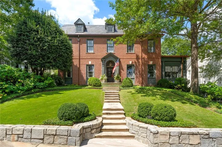 Brick colonial exterior with a stone retaining wall, stone staircase, and mature trees framing the property
