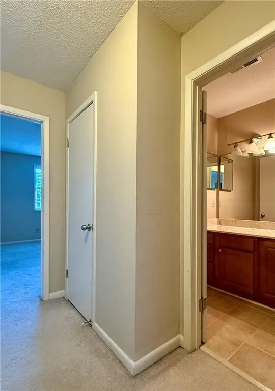 Corridor featuring a textured ceiling and light colored carpet