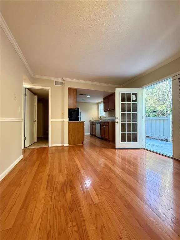 Unfurnished living room with crown molding, light wood finished floors, and a textured ceiling