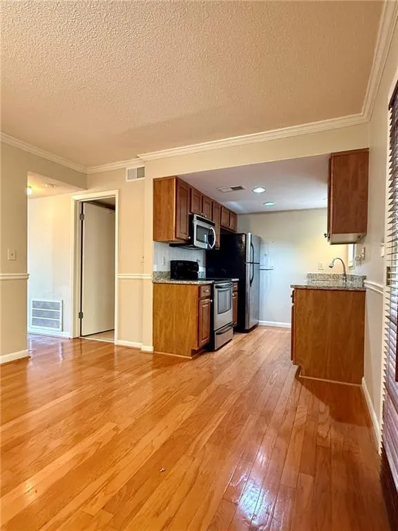 Kitchen with brown cabinetry, stainless steel electric stove, light stone countertops, crown molding, and light wood-style flooring