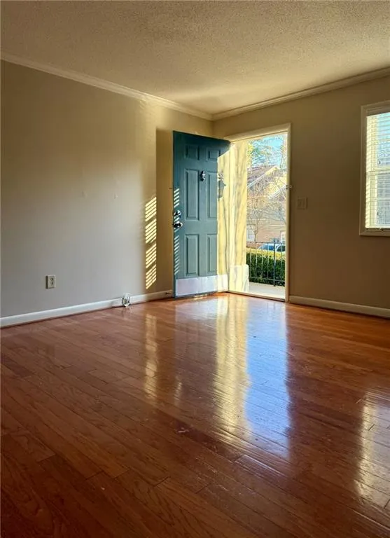 Empty room featuring hardwood / wood-style flooring, crown molding, and a textured ceiling