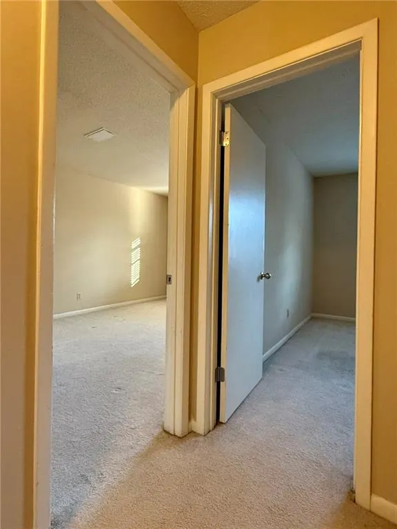 Corridor featuring a textured ceiling and light carpet