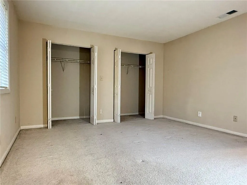 Unfurnished bedroom with two closets and light colored carpet