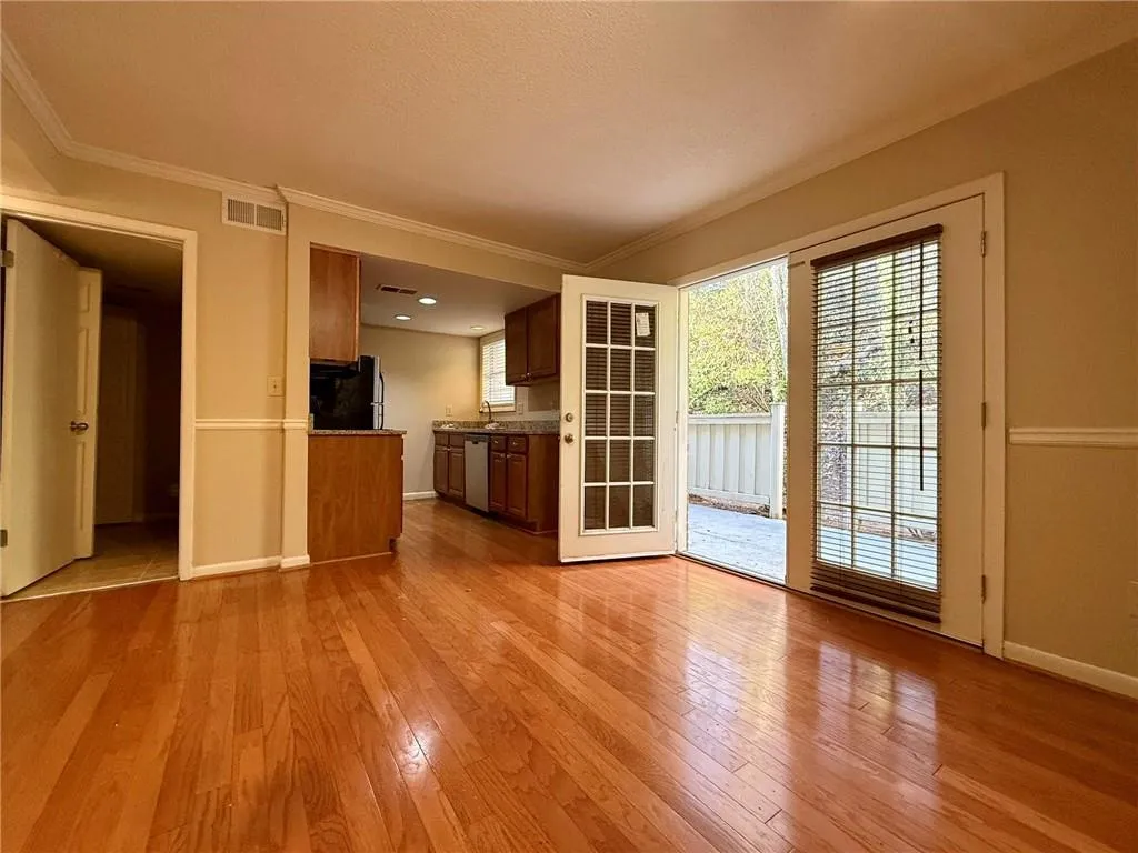 Kitchen featuring light wood-style flooring, ornamental molding, brown cabinetry, stainless steel dishwasher, and dark countertops