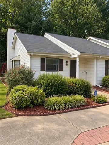 White siding exterior with dark shingle roofing, featuring a covered entry and a concrete driveway with brick paver accents