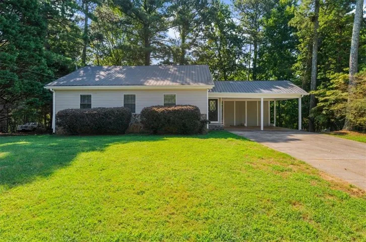 Single-story residence featuring light-colored siding, a metal roof, and a paved driveway leading to an attached carport