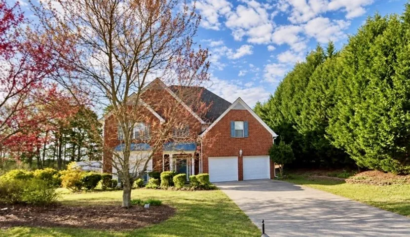 Brick exterior residence featuring a two-car garage, mature landscaping, and an expansive paved driveway