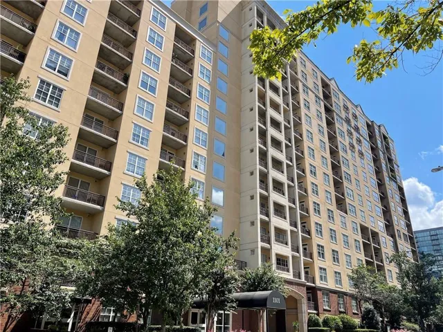 Multi-story building featuring a light-colored facade, numerous windows, and multiple balconies with dark railings