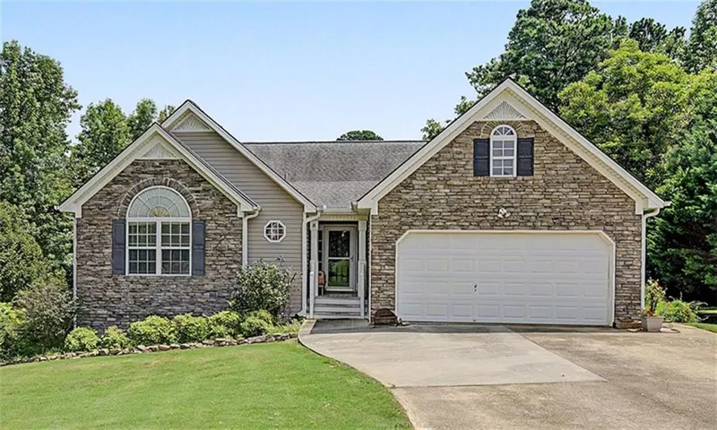 Stone and siding exterior with a two-car garage, arched window, and landscaped front yard