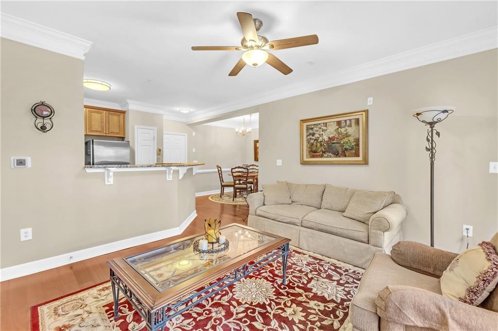 Living room with ceiling fan with notable chandelier, hardwood / wood-style floors, and ornamental molding