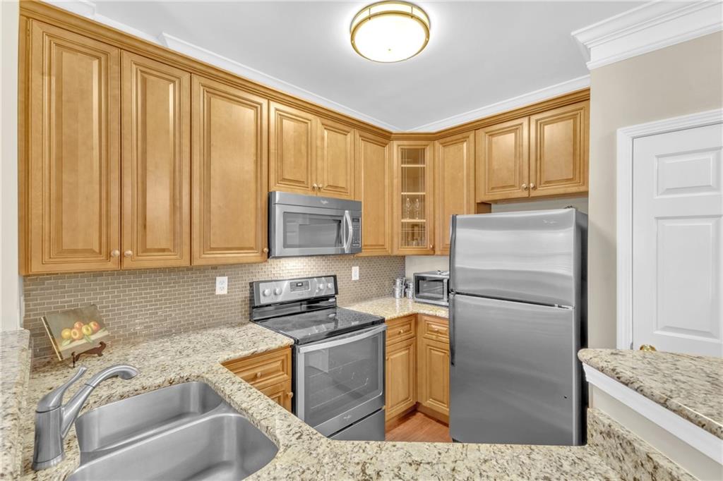 Kitchen with sink, appliances with stainless steel finishes, backsplash, and light stone counters