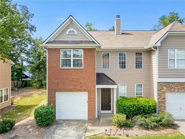 Brick and siding exterior with an attached garage, covered entryway, and mature landscaping