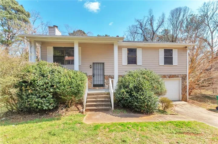 Bi-level home with stone siding, a garage, covered porch, concrete driveway, and a chimney