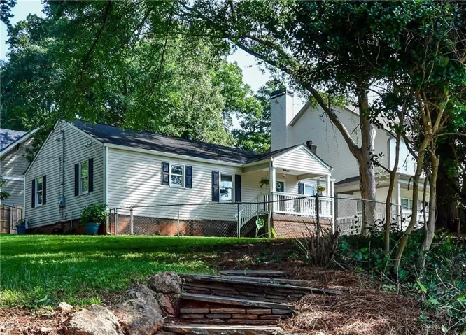 Traditional ranch-style residence featuring light-colored siding, dark shutters, and a covered front porch with white railings