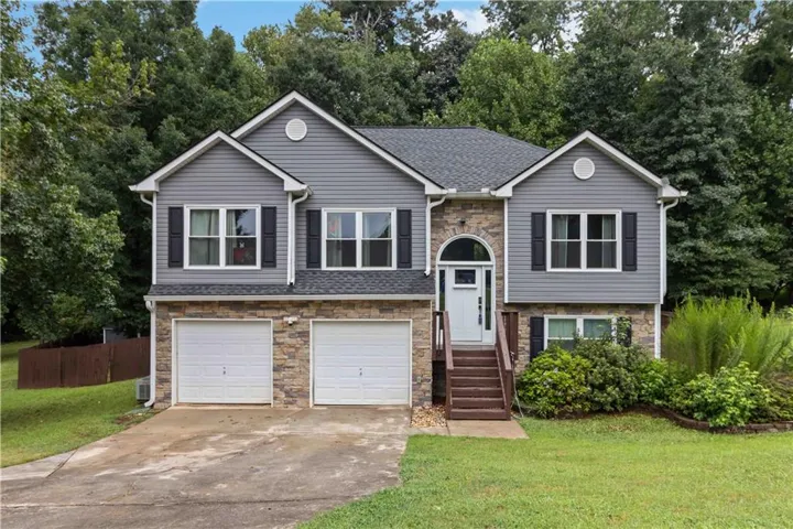 Two-story residence featuring a stone and siding exterior, dual garage doors, a covered entry with an arched transom, and mature landscaping