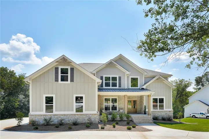 Two-story residence featuring light-toned vertical siding, stone accents, and a covered entry porch