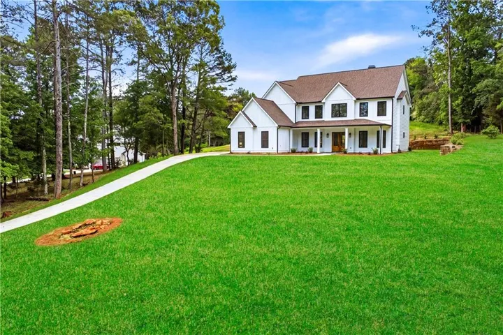 White siding exterior with a dark brown shingle roof, expansive green lawn, and a paved driveway