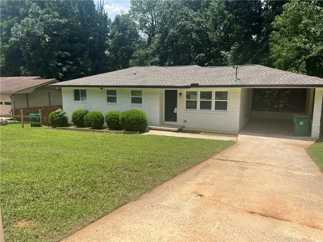 White brick exterior with a gray shingle roof, featuring a covered carport and a concrete driveway