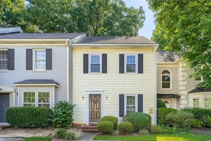 Two-story exterior with light-colored siding, black window shutters, a prominent front door, and established landscaping