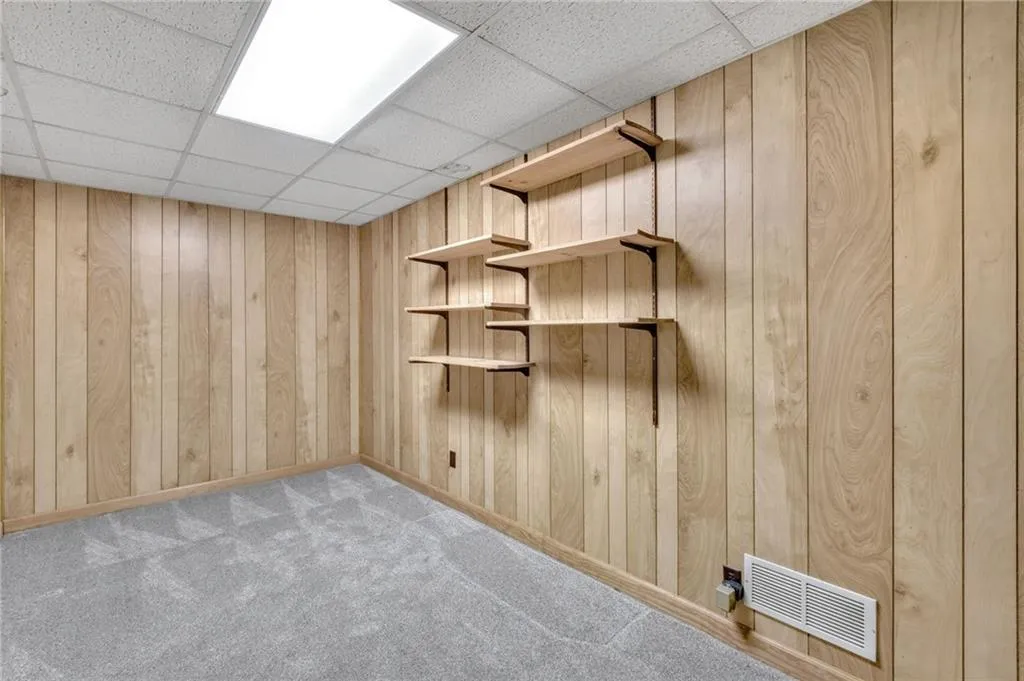 Spare room with wooden walls, visible vents, a drop ceiling, and light colored carpet