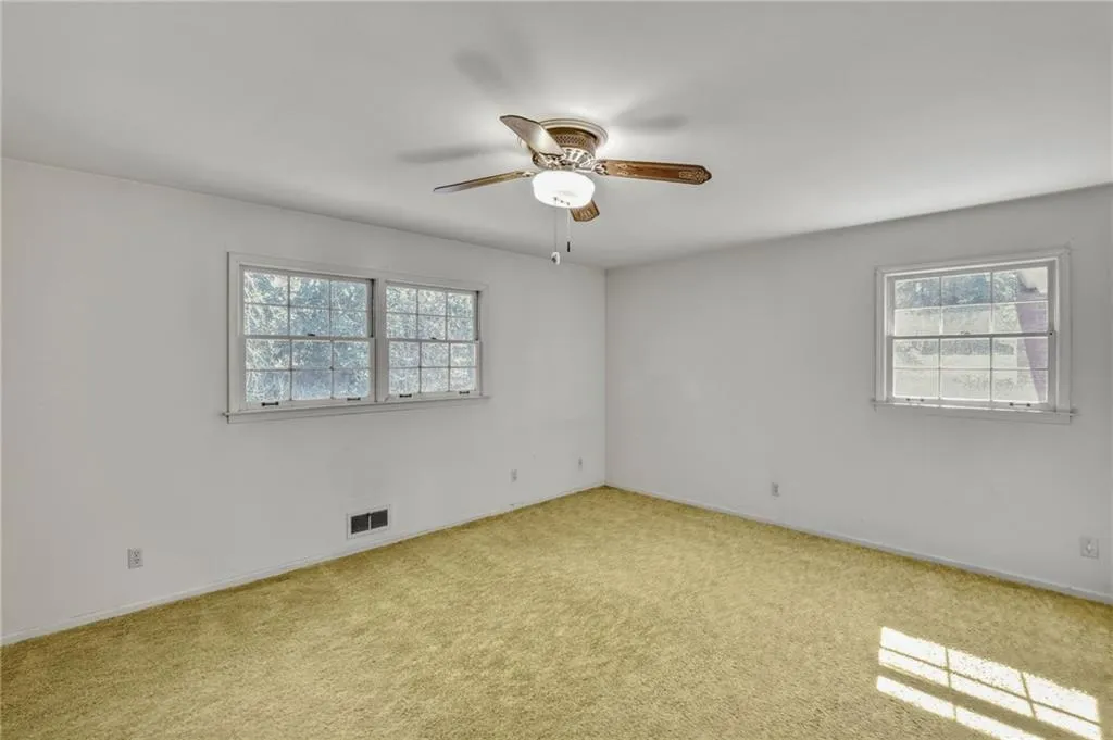 Empty room with ceiling fan, visible vents, and light colored carpet