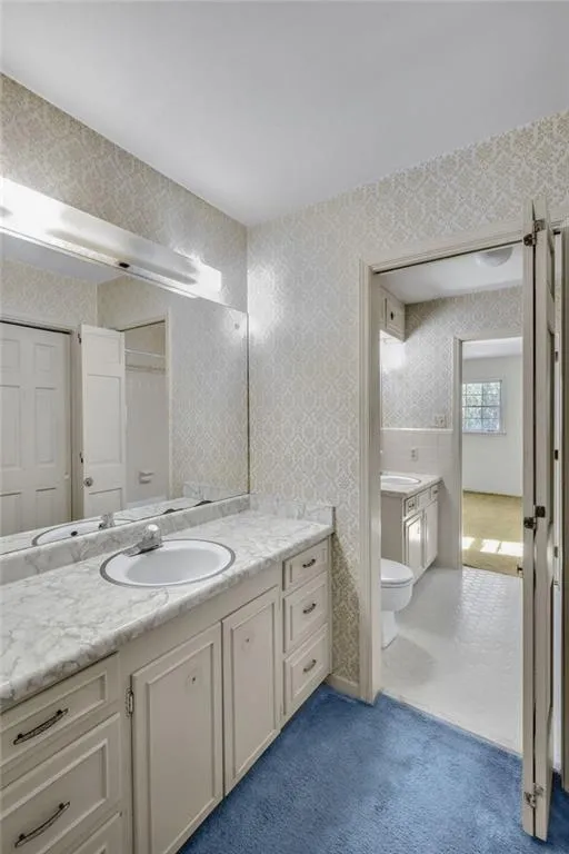 Bathroom with toilet, vanity, and wallpapered walls