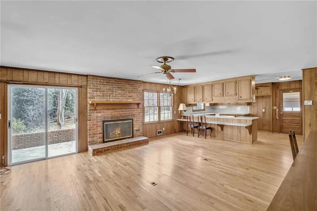 Unfurnished living room featuring wooden walls, visible vents, a ceiling fan, light wood-type flooring, and a fireplace