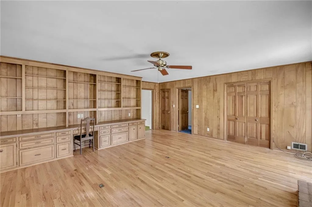 Unfurnished office with wooden walls, visible vents, a ceiling fan, built in study area, and light wood finished floors
