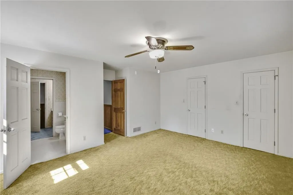 Unfurnished bedroom with light carpet, ceiling fan, connected bathroom, and visible vents