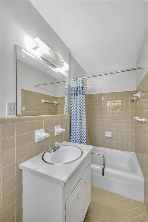 Full bathroom with shower / bath combination with curtain, vanity, and tile walls