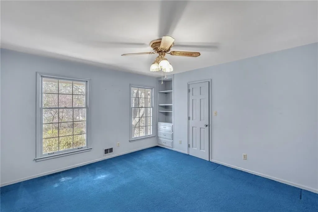 Empty room featuring visible vents, baseboards, a ceiling fan, dark colored carpet, and built in shelves