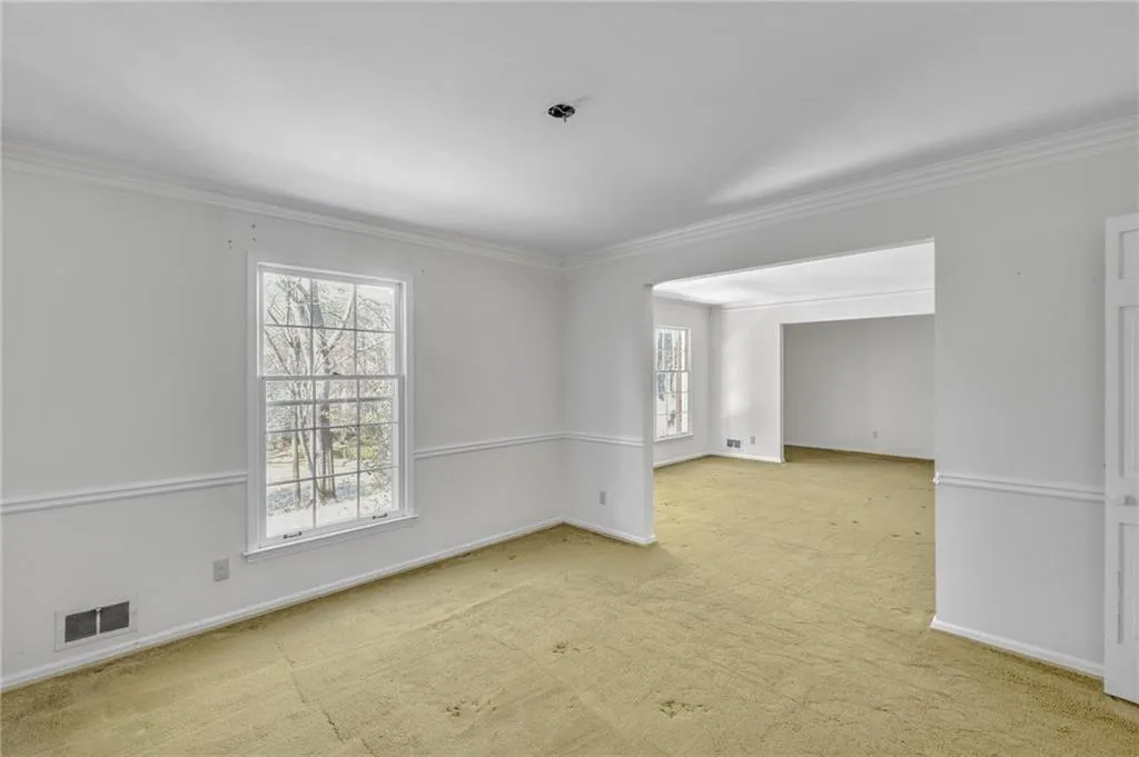 Spare room with a healthy amount of sunlight, visible vents, ornamental molding, and light colored carpet