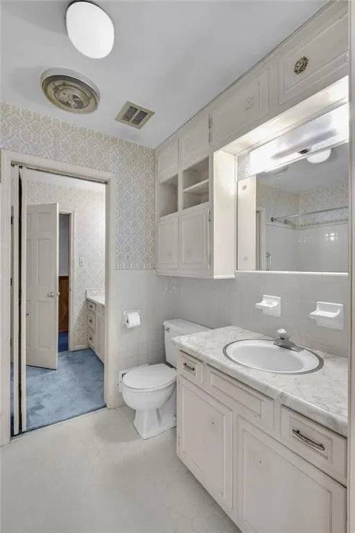 Bathroom with toilet, wallpapered walls, visible vents, and vanity