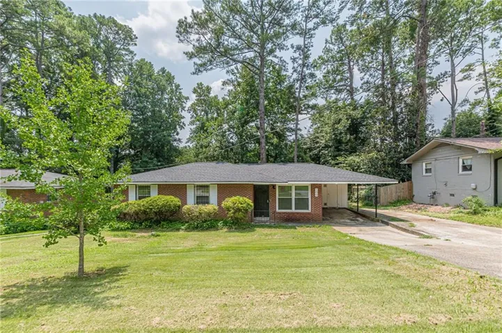 Brick ranch-style home featuring a covered carport, white window shutters, and a dark shingle roof