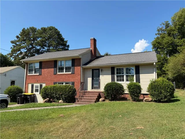 Brick and siding exterior with a dark gray shingle roof, featuring a prominent brick chimney, black window shutters, and a front entry with brick steps