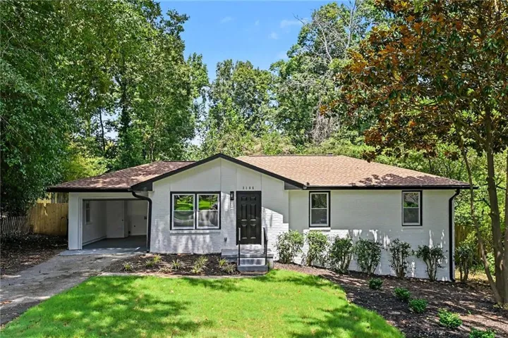 White brick exterior with a brown shingle roof, dark trim windows, and an attached carport