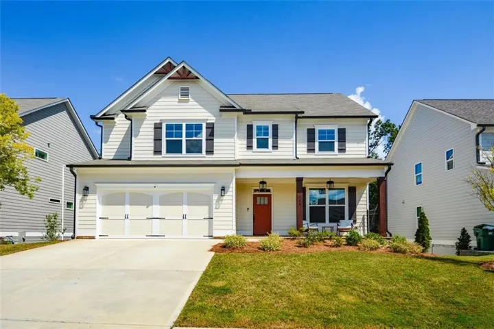Two-story residence featuring light-colored siding, a covered front porch with dark pillars, and a prominent red entry door