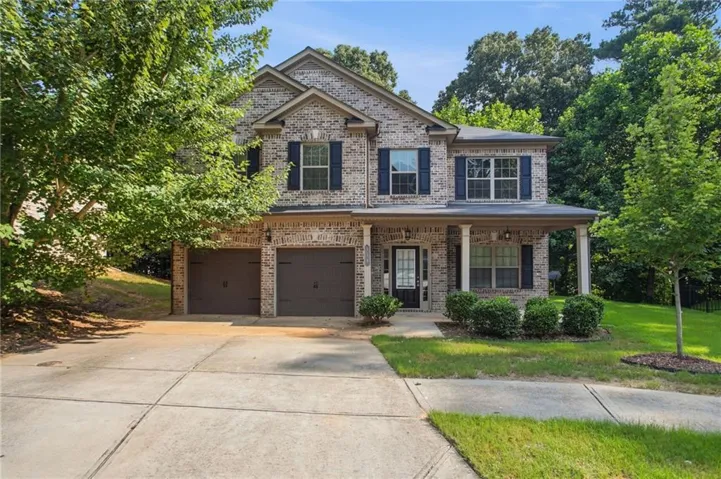 Traditional brick two-story residence featuring a covered front porch with white columns, a two-car garage, and dark shuttered windows
