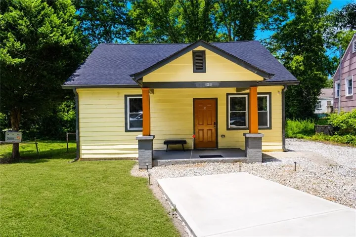 Single-story residence featuring a yellow siding exterior, dark blue shingle roof, and a covered front porch with wood columns on stone bases