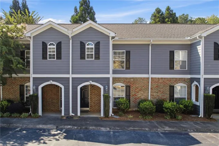 Townhome exterior featuring brick and siding facade, arched entryways, and upper-level arched windows with shutters