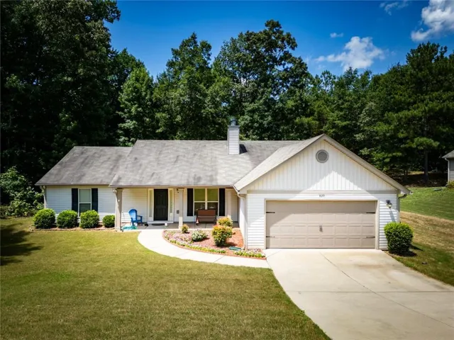 White exterior siding with dark shutters, front entry porch, attached garage with a light-colored door, concrete driveway, and a landscaped front yard with a curved pathway