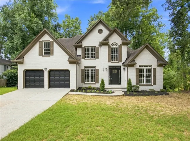 White brick exterior with dark brown trim, multiple gables, and a two-car garage
