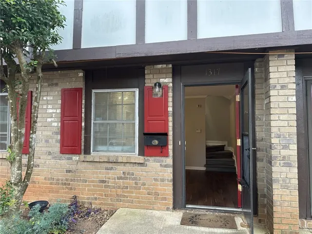 Brick exterior with red shutters, a prominent front door with house numbers, and a storm door