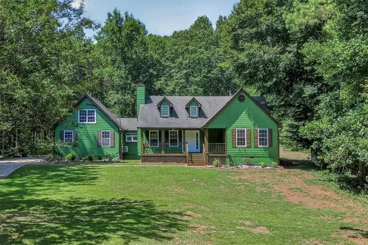 Spacious green exterior with white trim, a covered front porch, multiple dormer windows, a prominent chimney, and a gravel driveway