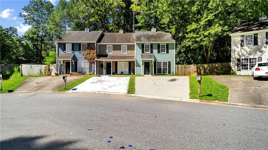 Colonial-style residence featuring a multi-car driveway with concrete surface, professional landscaping with mature trees and manicured lawn, brick and siding exterior with traditional architectural detailing, and a two-story structure with multiple windows and defined roofline