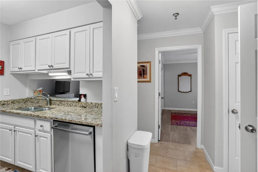 Kitchen with white cabinets, light stone countertops, crown molding, and dishwasher